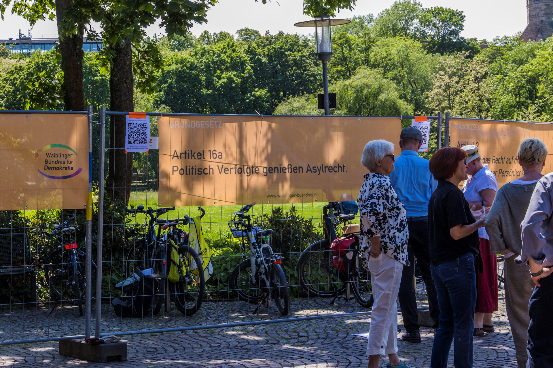 Menschen drängen sich imm Schatten - Banner mit GG Artikeln